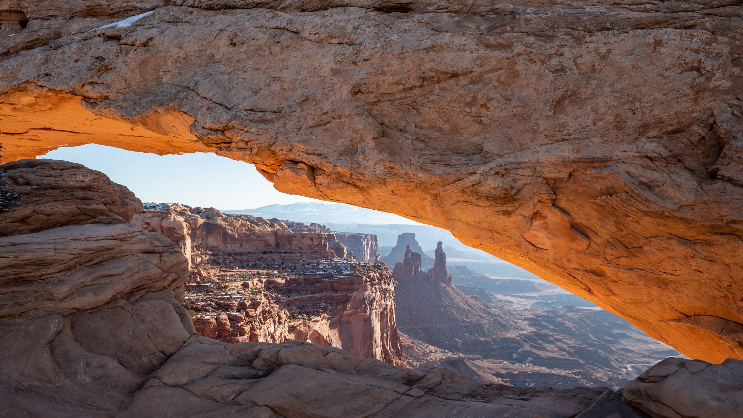 Sunrise view through Mesa Arch in Canyonlands National Park, Utah, with orange glow illuminating the arch and desert canyon landscape in the background.